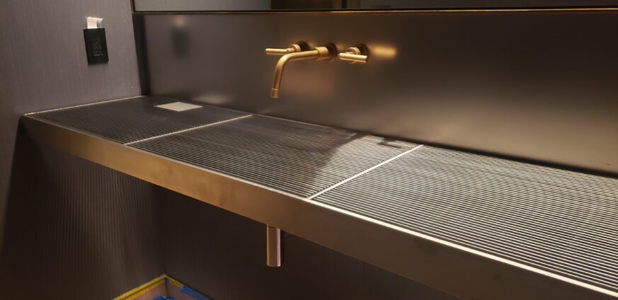 Powder Grate Sink and Vanity made of a sleek stainless steel and brass faucet and sconce for a touch of warmth.